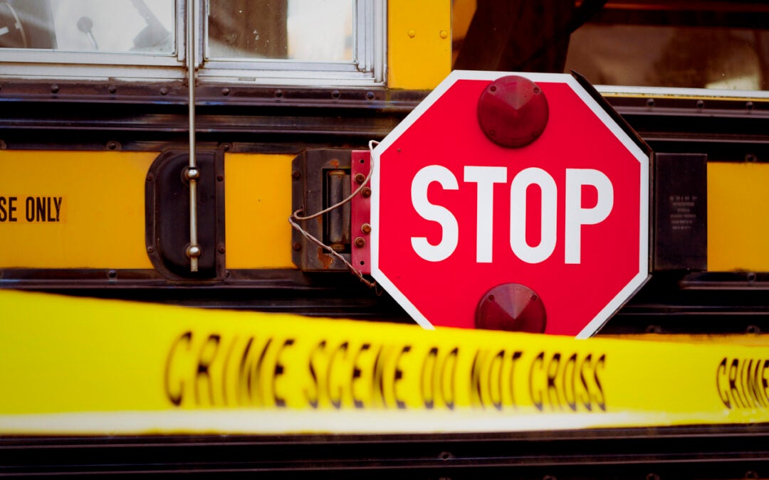 The side of a school bus with cordon tape that reads "CRIME SCENE DO NOT CROSS".