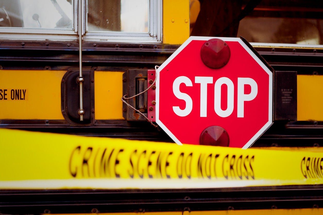 The side of a school bus with cordon tape that reads "CRIME SCENE DO NOT CROSS".