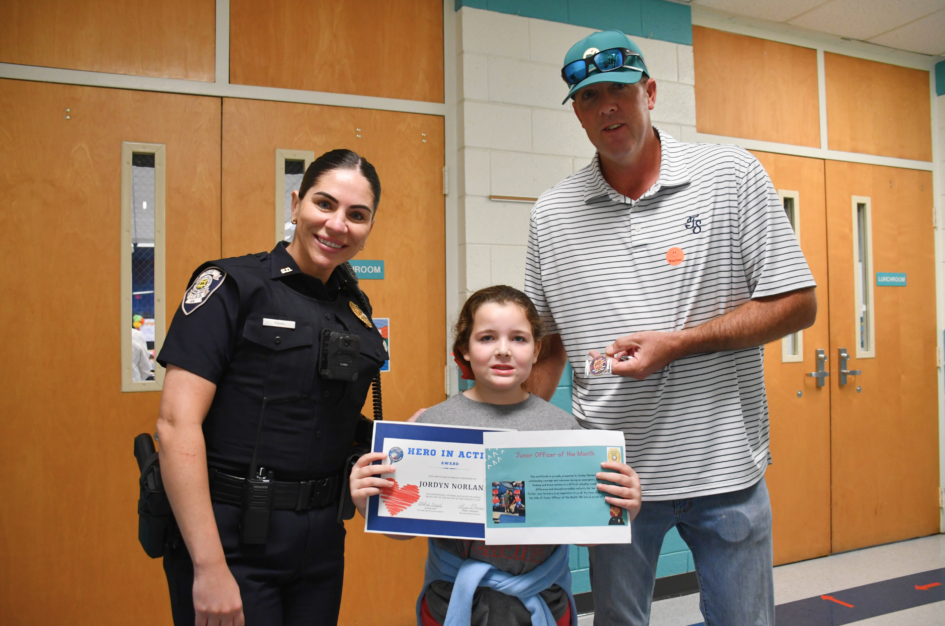 Riverside Elementary second grader Jordyn Norland is pictured with Officer Saal and her father, Mike, after being honored during the school’s Student of the Month event for calling 911 and helping save her mother’s life. Photo courtesy Columbia County School District