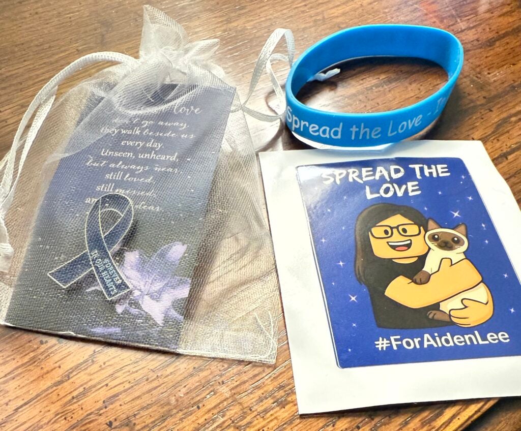 Each guest received a small bag containing a blue ribbon, “Spread the Love” wristband and sticker featuring artwork of Aiden Lee and his cat along with hashtag #ForAidenLee. Photo by Drew Wall