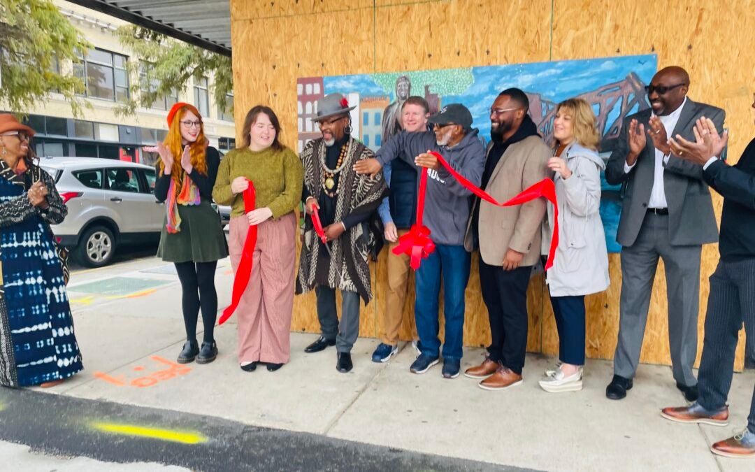 Group of people cutting ribbon at mural in downtown.