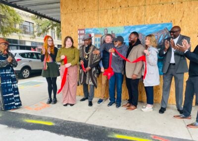 Group of people cutting ribbon at mural in downtown.
