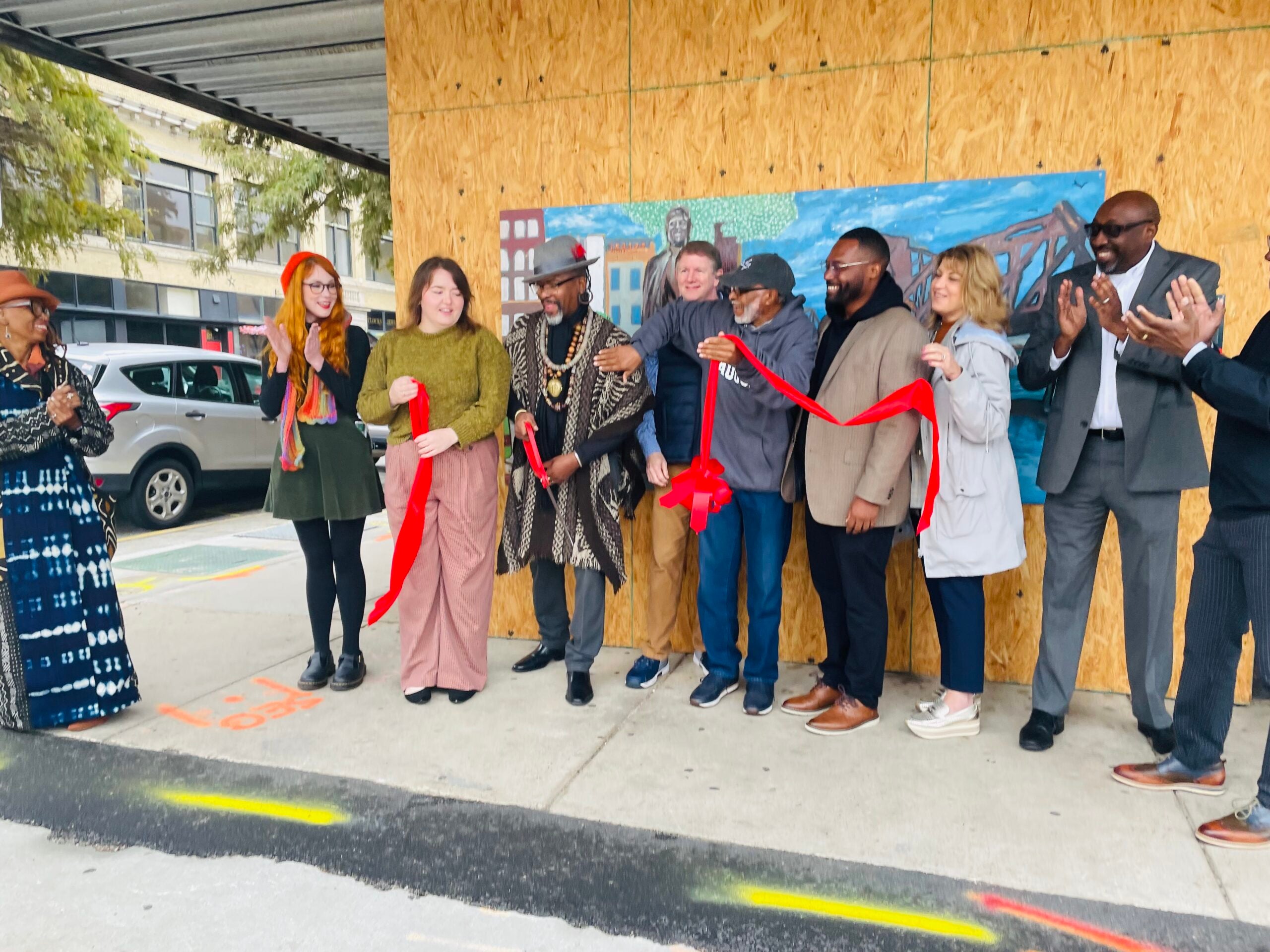 Group of people cutting ribbon at mural in downtown.