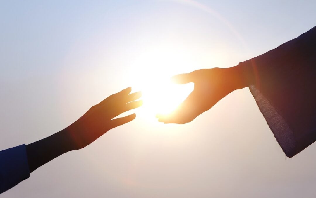 Hand of salvation, Christian hand reaching out to the hand of Jesus Christ, bright sun silhouette