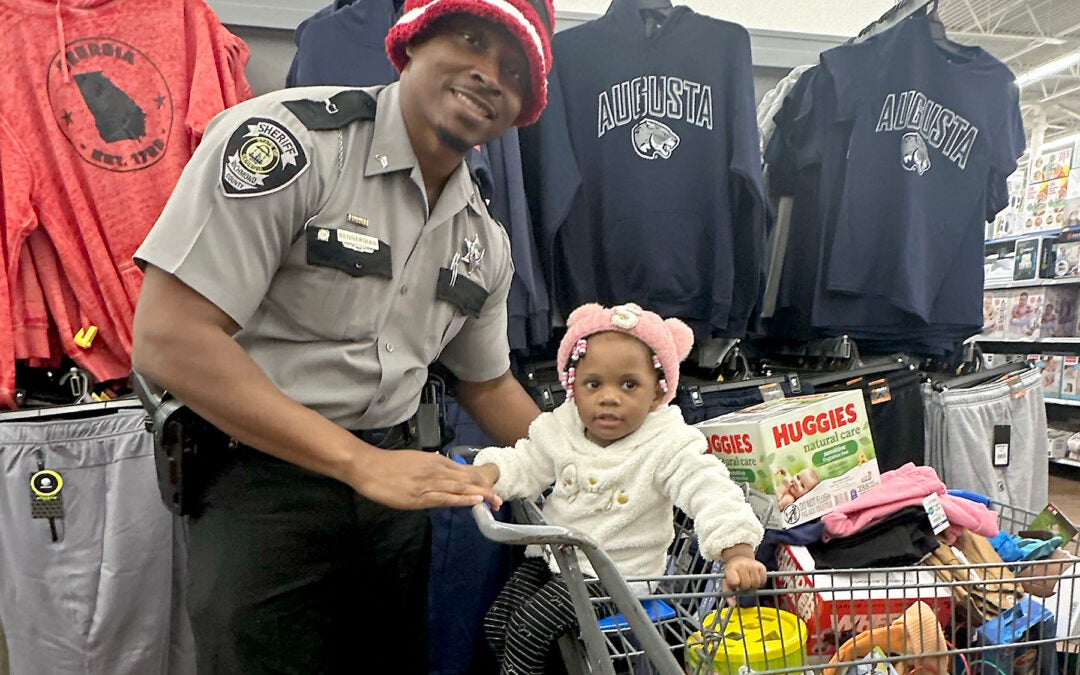 Cpl. Anthony Bennerman shopped with one-year-old Skylar Ivey and her mom Shaneka Ivey at the Wrightsboro Road Walmart during Richmond County Sheriff Gino Brantley's first-annual "Shop with a Cop" event Thursday. Staff photo by Susan McCord
