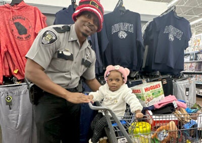 Cpl. Anthony Bennerman shopped with one-year-old Skylar Ivey and her mom Shaneka Ivey at the Wrightsboro Road Walmart during Richmond County Sheriff Gino Brantley's first-annual "Shop with a Cop" event Thursday. Staff photo by Susan McCord