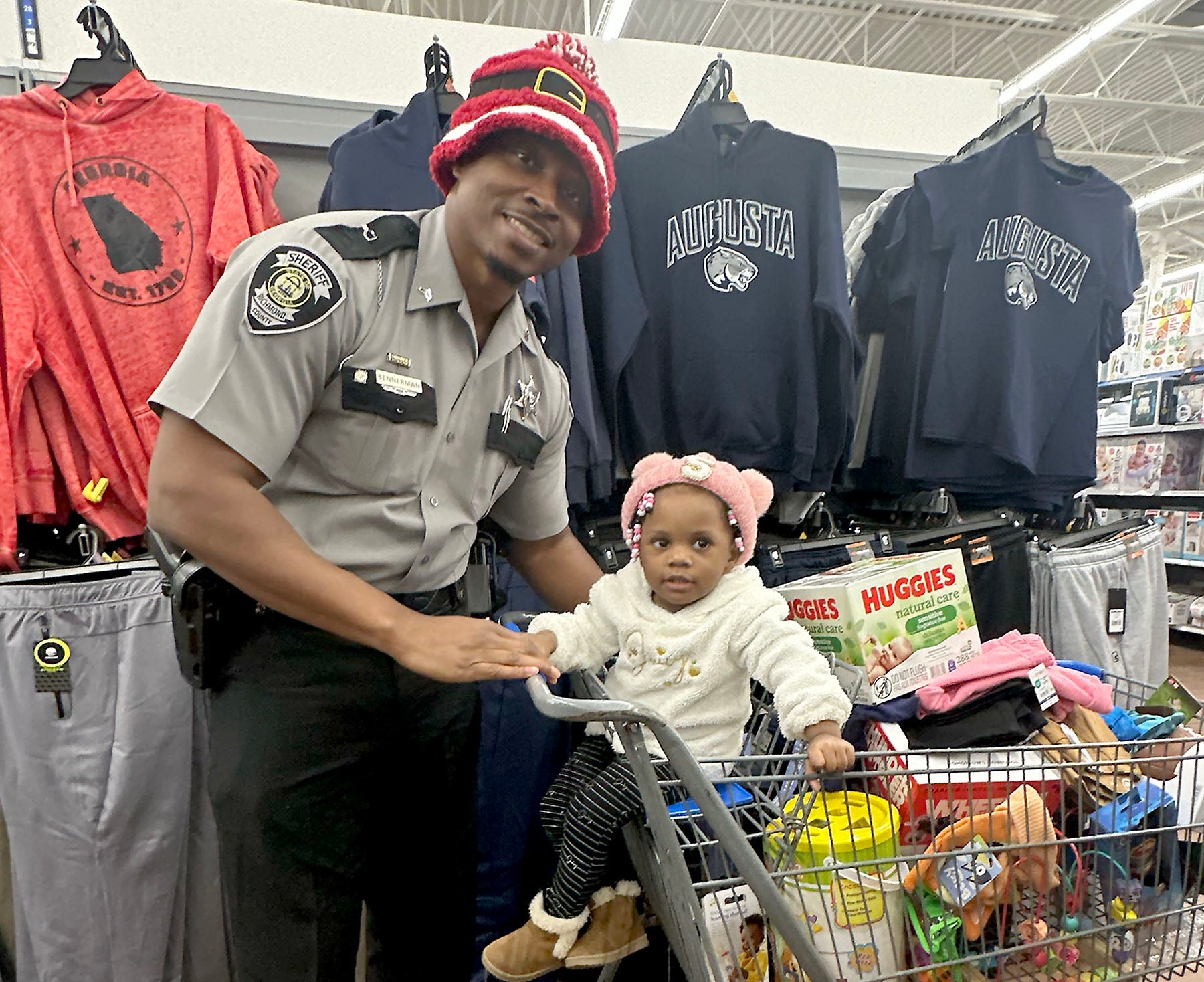 Cpl. Anthony Bennerman shopped with one-year-old Skylar Ivey and her mom Shaneka Ivey at the Wrightsboro Road Walmart during Richmond County Sheriff Gino Brantley's first-annual "Shop with a Cop" event Thursday. Staff photo by Susan McCord